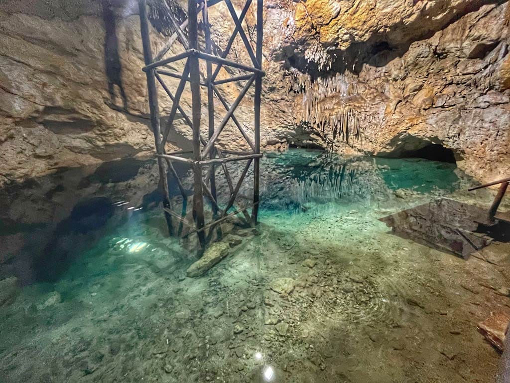 A tranquil underground cenote with clear water, rock formations, and a wooden structure under illumination, showcasing natural beauty and geological features.