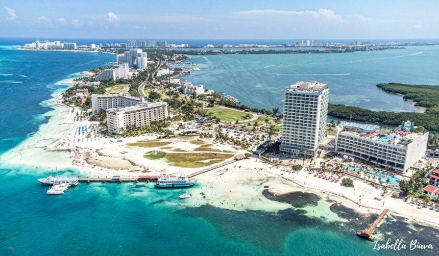 Aerial view of Cancun’s Hotel Zone peninsula, with a mix of beachfront resorts, turquoise ocean, white sandy shores, and Isla Mujeres visible in the distance.