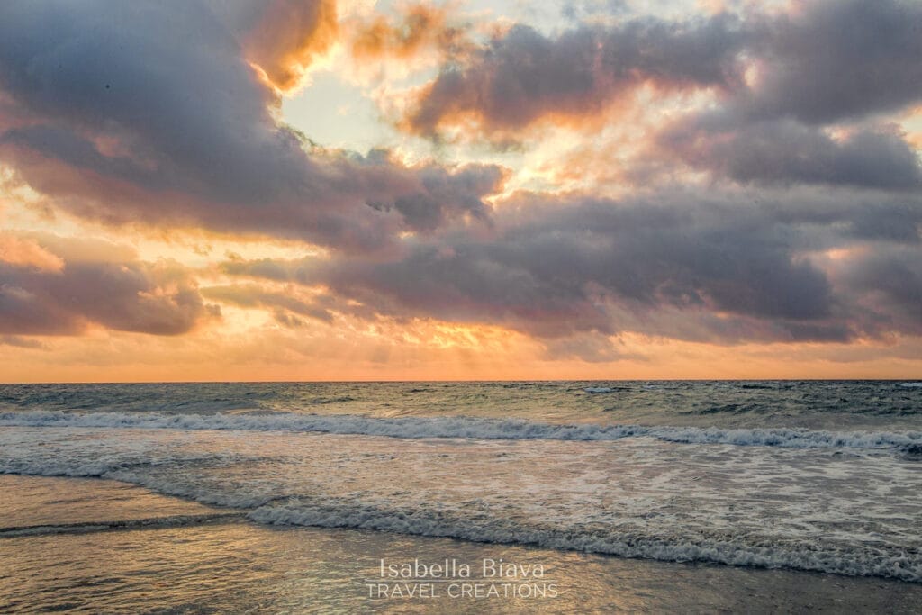 Early morning sunrise over Tulum Beach, with golden hues reflecting on the calm sea and silhouetted palm trees framing the horizon.
