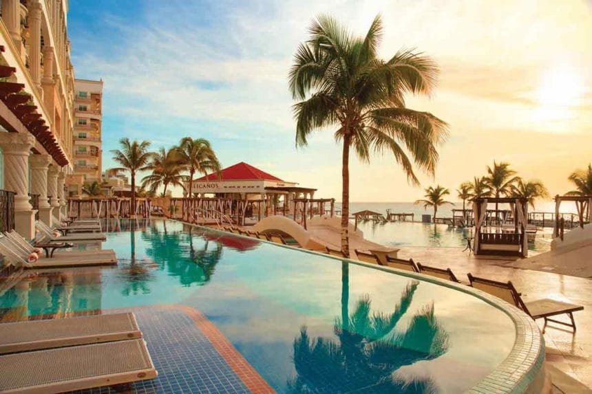 Poolside scene at Hyatt Zilara Cancun during golden hour, with sun loungers, a curved pool, palm trees, and the beach bar “Pelicanos” in the background.

