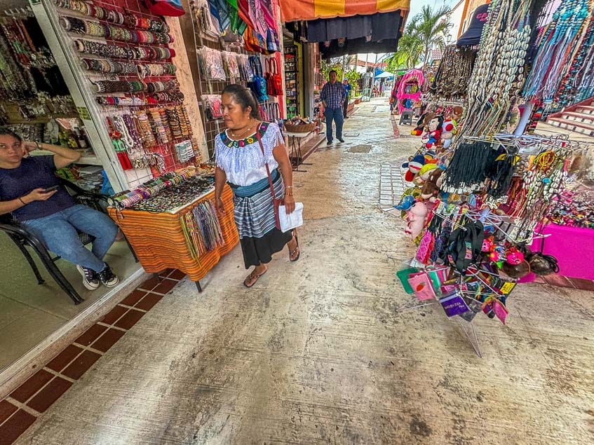 A vibrant market scene with colorful textiles and jewelry. People browse stalls filled with handmade crafts on a sunny day. No landmarks visible.