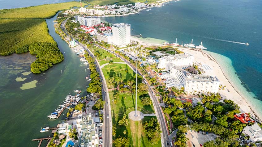 Aerial view of Cancun's hotel zone peninsula featuring beaches, high-rise hotels, and lush greenery surrounded by turquoise waters.