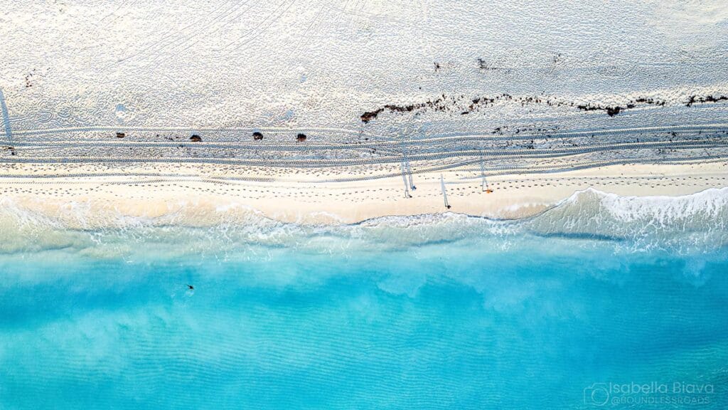 Aerial view of a serene beach with turquoise waves gently washing ashore, alongside empty sunbeds and umbrellas, creating a tranquil coastal scene.