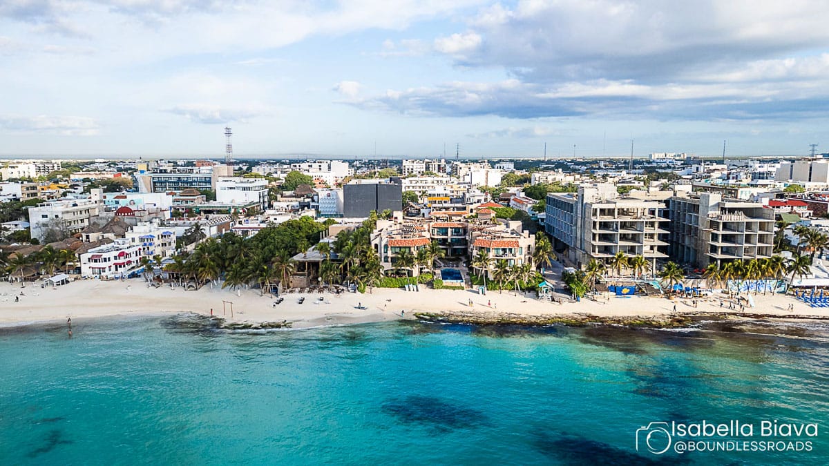Aerial view of a coastal city with beachfront, turquoise waters, and numerous buildings. People on the beach enjoy the sunny weather.