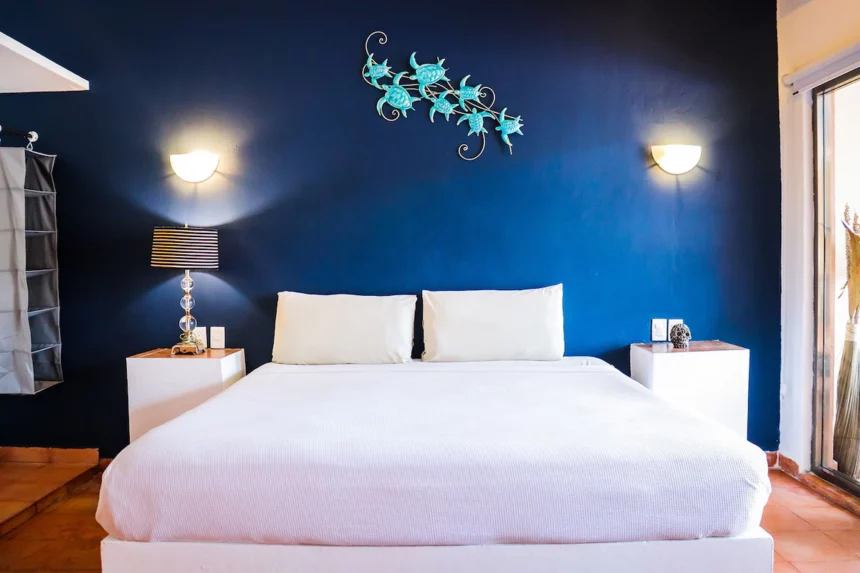white bed against a dark blue wall and a light blue turtle decoration above the bed